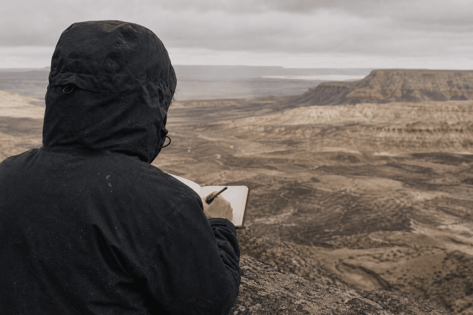 An anonymous person takes notes while facing an open landscape.